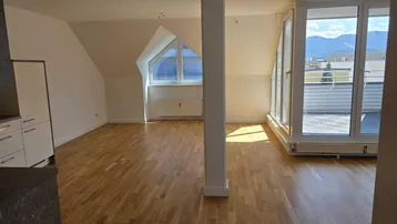 Heller Wohnbereich im Dachgeschoss mit Holzboden, Zugang zur Terrasse und Bergblick.