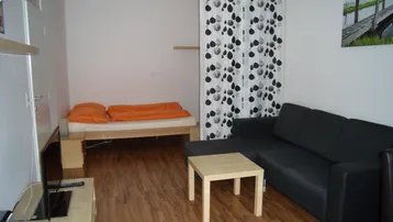 Gemütlicher Wohnbereich mit Schlafgelegenheit, Holzboden und einem Sofa, ideal für ein Studio-Apartment.
