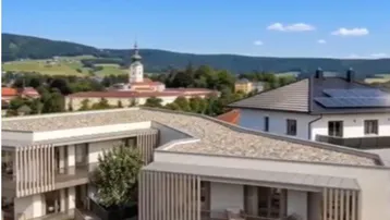 Moderne Wohngebäude mit Balkonen und Blick auf ein historisches Dorf und grüne Hügel.
