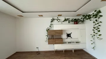 Geräumiges Wohnzimmer mit Laminatboden, moderner TV-Wand und indirekter Deckenbeleuchtung.