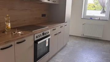 Moderne Einbauküche mit beigefarbenen Schränken, Holzarbeitsplatte und Induktionskochfeld.