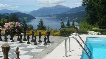 Außenbereich mit Pool, großem Schachspiel und atemberaubendem Blick auf den See und die Berge.