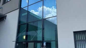 Moderne Gebäudefassade mit großer Glasfront und Eingangsbereich unter blauem Himmel.