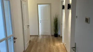 Heller Flur mit Laminatboden und modernen Wandleuchten, der zu verschiedenen Räumen führt.