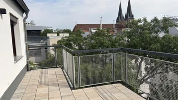Geräumige Dachterrasse mit Fliesenboden und Blick auf die Stadt und Kirchtürme.