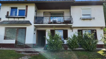 Fassade eines Hauses mit Balkon, Rollläden an den Fenstern und einem kleinen Vorgartenbereich.