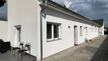 Moderne weiße Hausfassade mit kleiner gepflasterter Terrasse und Sitzgelegenheiten im Freien.
