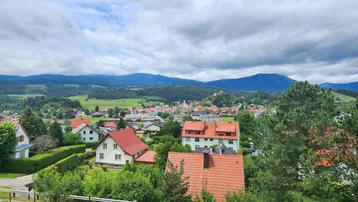 Weitblick vom Balkon über ein Dorf, grüne Hügel und eine malerische Berglandschaft in der Ferne.