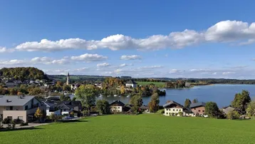 Malerische Ansicht eines Dorfes am Seeufer mit grünen Wiesen und blauem Himmel.