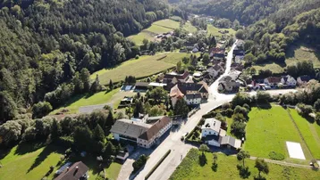 Weitläufige Luftaufnahme eines malerischen Dorfes eingebettet in eine grüne Hügellandschaft.