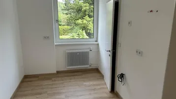 Helles Zimmer mit Laminatboden und Fenster mit Blick ins Grüne, ideal als Schlaf- oder Arbeitszimmer.