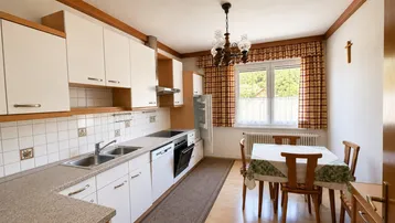 Traditionelle Küche mit weißen Schränken, Fliesenrückwand und Essbereich am Fenster.