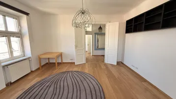 Helles Zimmer mit Parkettboden, dekorativer Deckenleuchte und Zugang zu weiteren Räumen.