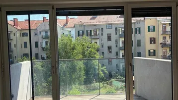 Blick vom Wohnzimmer auf den Balkon und die umliegenden Gebäude mit viel Grün.