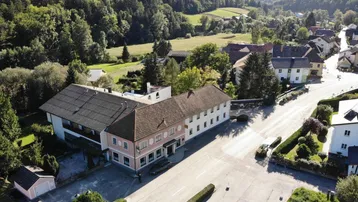 Luftaufnahme eines Dorfes mit einem großen Gebäude und umliegender grüner Hügellandschaft.