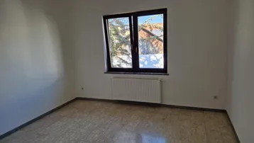 Leerer Raum mit Fenster, Blick ins Grüne und Heizkörper unter dem Fenster.