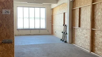 Leerer Lagerraum mit OSB-Trennwänden, Betonboden und großen Fenstern für natürliches Licht.