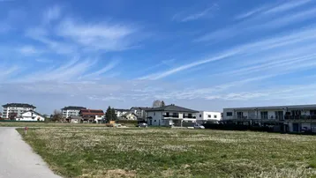 Weitläufiges unbebautes Grundstück mit Blick auf moderne Wohngebäude unter blauem Himmel.