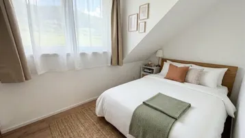 Helles Schlafzimmer im Dachgeschoss mit Dachschrägen, Holzboden und Bergblick aus dem Fenster.