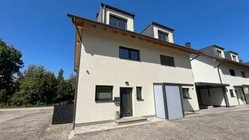 Modernes Reihenhaus mit heller Fassade, Satteldach und Carport im Freien.