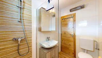 Modernes Badezimmer mit Duschbereich, Waschbecken und WC, ausgestattet mit hellen Fliesen und Holzelementen.