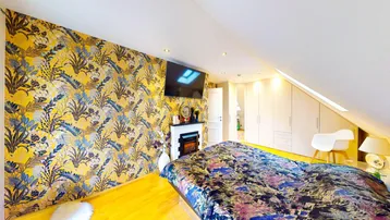 Gemütliches Schlafzimmer im Dachgeschoss mit auffälliger floraler Tapete und einem Elektrokamin.