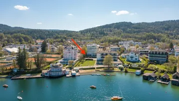 Luftaufnahme einer Stadt am See mit Bergen im Hintergrund und einem markierten Gebäude.