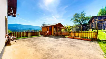 Sonniger Terrassenbereich mit Gartenhaus, Holzzaun und weitem Blick auf die Berge.