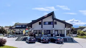 Modernes Geschäftsgebäude mit Parkplätzen und schrägem Dach in einer ländlichen Umgebung.