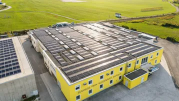 Luftaufnahme eines gelben Geschäftsgebäudes mit Solarpaneelen auf dem Dach, angrenzend an einen Flughafen.