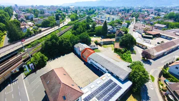 Luftaufnahme eines Gewerbeobjekts mit mehreren Gebäuden, großem Parkplatz und Solaranlage auf dem Dach.