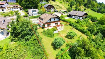 Luftaufnahme eines Hauses mit großem Grundstück und umgebender grüner Hügellandschaft.