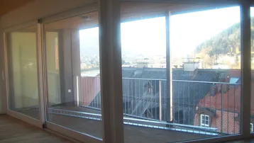 Helles Zimmer mit großen Glasfronten, Holzboden und Zugang zu einem Balkon mit Flussblick.