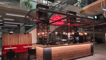 Moderne Bar mit Holzverkleidung, rotem Neonlicht und bequemen Sitzgelegenheiten in einem Einkaufszentrum.
