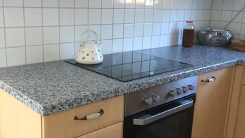 Funktionale Küche mit hellen Holzschränken, Granitarbeitsplatte und integriertem Induktionskochfeld und Backofen.