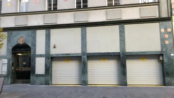 Gebäudefassade mit drei Garagentoren und einem eleganten Eingangsbereich, verziert mit Marmorplatten.