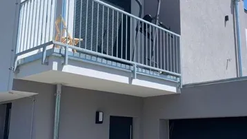 Moderne Hausfassade in Grau mit Balkon und integrierter Garage unter blauem Himmel.