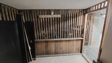 Innenraum im Rohbau mit freiliegenden Holzlattenwänden und Betonboden, bereit für den Ausbau.