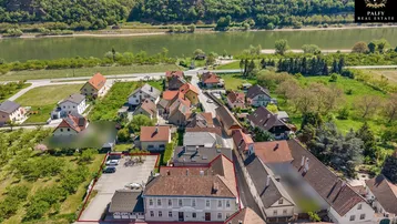 Luftaufnahme eines Dorfes mit Häusern, einem Fluss und grünen Hügeln im Hintergrund.