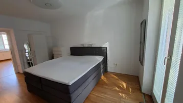 Helles Schlafzimmer mit Holzboden, einem Bett und Zugang zu einem weiteren Raum.