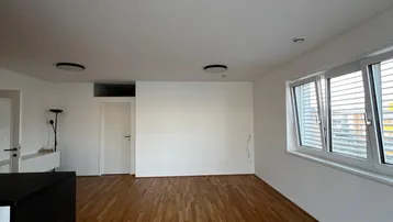 Helles Zimmer mit Holzboden und großen Fenstern, bereit zur Einrichtung.
