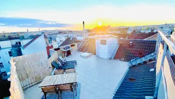 Geräumige Dachterrasse mit Sitzgelegenheiten, Liegestühlen und weitem Blick über die Stadt bei Sonnenuntergang.