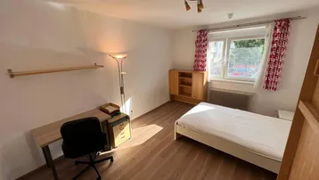 Helles Schlafzimmer mit Holzboden, Einzelbett, Schreibtisch und Fenster mit Blick ins Grüne.