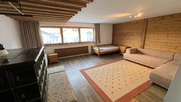 Gemütlicher Wohnbereich mit Holzwänden, Holzbalkendecke und traditionellem Kachelofen.