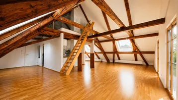 Geräumiger, heller Dachbodenraum mit sichtbaren Holzbalken, Holzfußboden und Zugang zu einem Balkon.