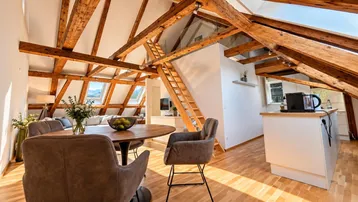 Heller offener Wohn- und Essbereich mit Holzbalken, Dachschrägen und Bergblick durch die Dachfenster.