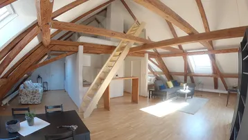 Geräumiger offener Wohn- und Essbereich mit sichtbaren Holzbalken und viel Tageslicht durch Dachfenster.