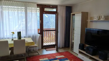 Heller Wohn- und Essbereich mit Holzboden, Teppich und Zugang zu einem Balkon mit Bergblick.