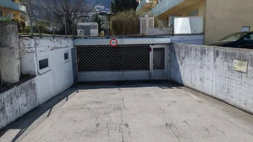 Einfahrt zu einer Tiefgarage mit Rolltor und umliegenden Gebäuden unter klarem Himmel.