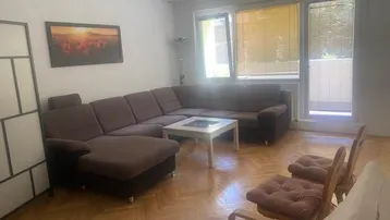 Gemütliches Wohnzimmer mit großem Ecksofa, Parkettboden und Zugang zu einem Balkon.